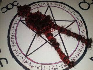 Muñeco atado con hilo rojo y negro sobre un pentáculo dibujado con runas