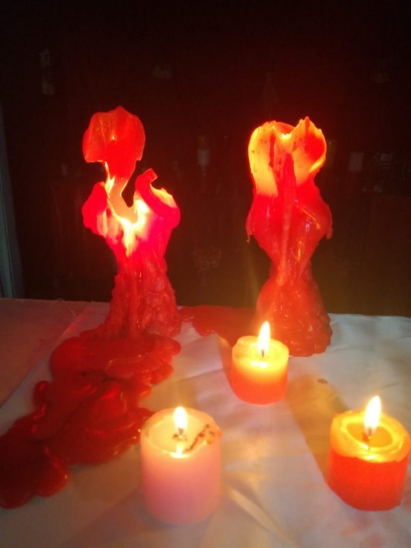 Dos velas rojas de figura derritiéndose encendidas, con velas pequeñas alrededor sobre un paño blanco