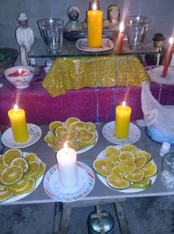 Altar de prosperidad con velas amarillas y blancas, platos de naranjas en rodajas y figuras de santos