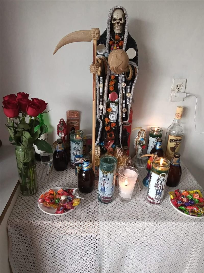 Altar con figura de la Santa Muerte, velas encendidas, rosas rojas y ofrendas