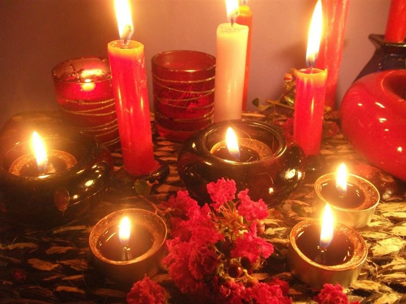 Velas rojas y blancas encendidas junto a lamparillas y flores rosadas